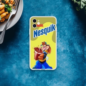 Puede incluir: Una funda de teléfono con el logotipo de Nesquik y un personaje de dibujos animados. La funda tiene un fondo amarillo con el logotipo de Nesquik en azul y blanco. El personaje de dibujos animados sostiene un vaso de leche con chocolate. La funda tiene un borde blanco.