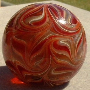 May include: A red, white, and brown swirl glass marble. The marble has a glossy finish.