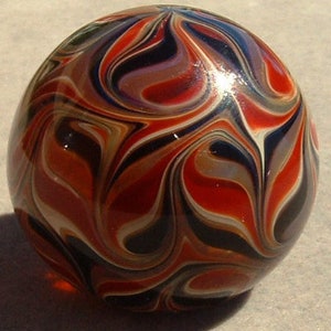 May include: A glass marble with a swirling pattern of red, white, black, and brown.