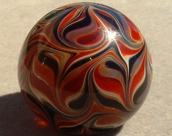 May include: A glass marble with a swirling pattern of red, white, black, and brown.