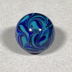 May include: A blue and teal glass marble with a swirling pattern. The marble has a glossy finish and a subtle sparkle.