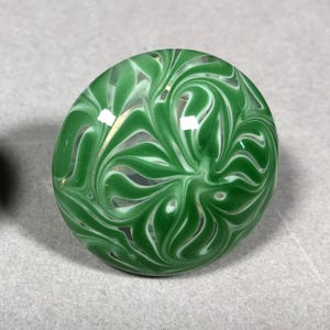 May include: A green glass marble with white swirls. The marble has a glossy finish.