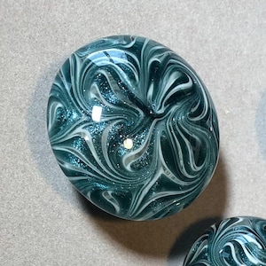 May include: A teal blue glass paperweight with white swirls and glitter.