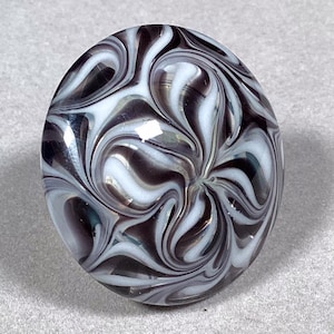 May include: A round glass paperweight with a swirling black and white pattern. The glass is iridescent and has a glossy finish.