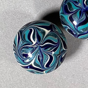 May include: Two blue, white, and black glass marbles with a swirling pattern. The marbles have a glittery finish.