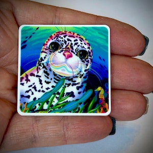 May include: A square sticker featuring a colorful illustration of a seal with large, expressive eyes. The seal has a spotted pattern and is set against a vibrant underwater scene with seaweed and a seahorse. The color palette includes blues, greens, and pinks.