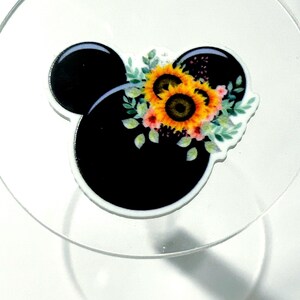 May include: A black silhouette of a mouse head shape featuring a cluster of yellow sunflowers, green leaves, and small pink flowers arranged on the right side. The design is printed on a smooth, glossy surface with a white border outline.
