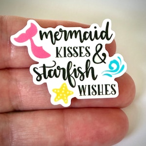 May include: A white sticker with the words "mermaid kisses & starfish wishes" in black script. The sticker features a pink mermaid tail, a yellow starfish, and blue wave accents.
