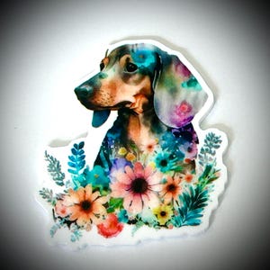 May include: A sticker featuring a watercolor illustration of a dachshund dog with a floral design. The dog has a brown, black, and blue coat, and the flowers are in shades of pink, orange, blue, and yellow.