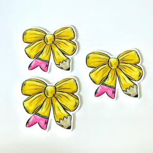 May include: Three yellow bow stickers with pencil designs. Each bow is a bright yellow color with a pencil tip in pink and gray. The stickers have a white border and are arranged on a white background.