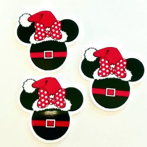 May include: Three black and white Mickey Mouse head-shaped ornaments with a Santa Claus theme. Each ornament features a red Santa hat, a red and white polka dot bow, and a black body with a red belt and white trim. The ornaments are on a white background.