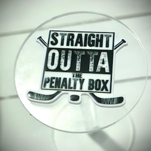 May include: A white sticker with black text and hockey stick graphics. The text reads "Straight Outta The Penalty Box".