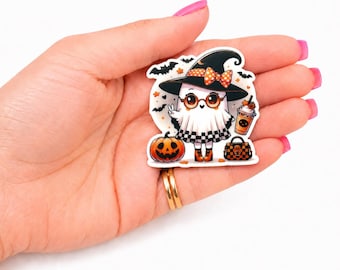 May include: A die-cut sticker featuring a cartoon ghost wearing a black witch hat with an orange polka-dot bow, round glasses, and orange boots. The ghost holds a coffee cup, stands next to a jack-o'-lantern, and carries a checkered handbag.