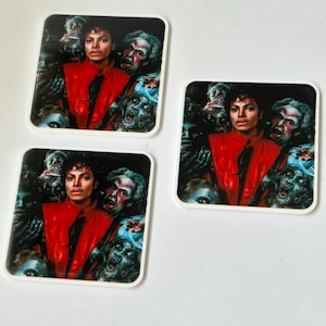 May include: Three square stickers featuring a portrait of Michael Jackson in a red jacket and black tie, surrounded by zombies. The stickers have a white border and are set against a white background.