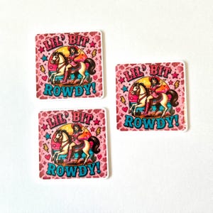 May include: Three square stickers featuring a cowgirl riding a horse against a sunset background. The design includes a pink cow print border, yellow lightning bolts, stars, and the text LIL' BIT ROWDY! in bold blue letters on each sticker.