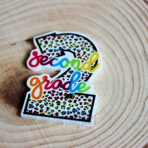 May include: A white number two with a colorful leopard print design. The words "second grade" are written in rainbow colors around the number.