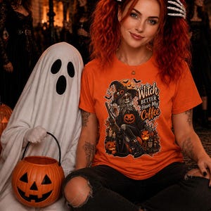 May include: An orange short-sleeved t-shirt featuring a graphic print of a skeleton wearing a witch hat and holding a coffee cup. The text "Witch Better Have My Coffee" is printed in a stylised font above pumpkins, bats, and candles.