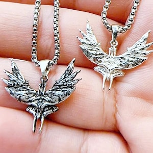 May include: Two silver-colored pendant necklaces. Each necklace features a detailed phoenix pendant with outstretched wings, suspended from a delicate chain. The pendants are intricately designed, showcasing the bird's feathers and form.