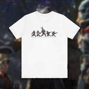May include: White t-shirt with a graphic of five cartoon figures wearing black and orange armor, holding weapons and running in a line. The figures are in a pixelated style.