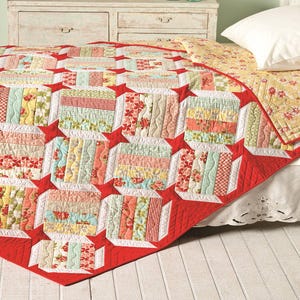 May include: A red, white, and green patchwork quilt with a geometric pattern. The quilt is made of various fabrics with floral and geometric designs. It is folded and displayed on a bed.