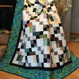May include: A patchwork quilt with a black and white checkered pattern, green and orange accents, and a teal border. The quilt is made of fabric with a batik design.