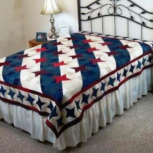 May include: A red, white, and blue quilt with a star pattern. The quilt is made with a variety of fabrics and has a ruffled edge.