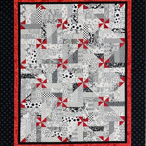 Puede incluir: Una colcha en blanco y negro con detalles de molinetes rojos. La colcha est&aacute; hecha de varias telas con diferentes patrones, incluyendo lunares, rayas y remolinos. La colcha est&aacute; enmarcada con un borde de lunares blancos y negros.