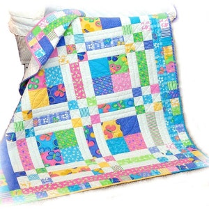 May include: A colourful patchwork quilt with a butterfly pattern. The quilt is made of various fabrics in shades of blue, pink, yellow, and green. The quilt is folded and displayed on a white surface.