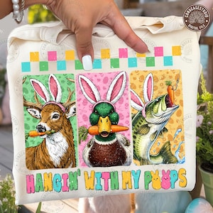 May include: A cream-colored sweatshirt featuring three panels with animal illustrations wearing bunny ears and holding carrots. The animals are a deer, a duck, and a fish. The text "HANGIN' WITH MY PEEPS" is printed at the bottom.