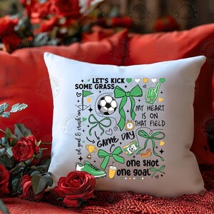 Puede incluir: Coj&iacute;n cuadrado blanco con tem&aacute;tica de f&uacute;tbol. El coj&iacute;n presenta un bal&oacute;n de f&uacute;tbol, lazos verdes y el texto "Let's Kick Some Grass", "Game Day" y "My Heart Is On That Field". Otros gr&aacute;ficos incluyen una bota de f&uacute;tbol, un trofeo y una bebida.