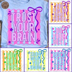 May include: A light blue t-shirt with the words "TRUST YOUR BRAIN" in large pink letters. The design includes a pink and purple striped frame, stars, and a purple bow. Additional designs with motivational phrases are also shown.