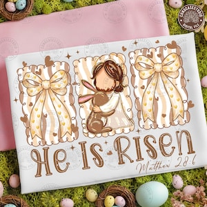 May include: White Easter-themed design featuring a central illustration of a figure embracing a bunny, flanked by decorative bows. The text "He Is Risen" and "Matthew 28:6" are displayed in brown script. The design incorporates hearts and stars.