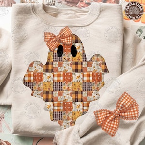 May include: A beige sweatshirt featuring a patchwork ghost design with a gingham bow. The ghost is made of various orange, brown, and yellow patterned squares. A matching bow is also visible. The design is perfect for Halloween.