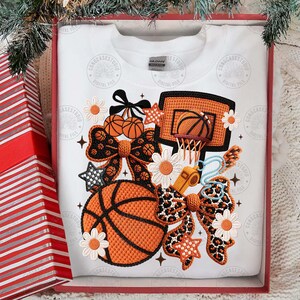 May include: White sweatshirt featuring a basketball design. The design includes an orange basketball, a hoop, bows, stars, and daisies. The design also includes a whistle and the text "CONGCASESTUDIO DIGITAL FILE".