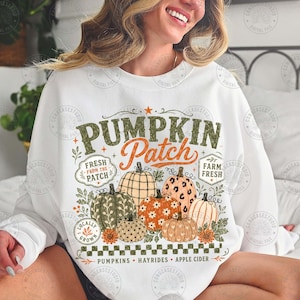 Peut inclure: Un sweat-shirt blanc &agrave; manches longues avec une impression graphique portant le texte PUMPKIN Patch, FRESH FROM THE PATCH, FARM FRESH, LOCALLY GROWN, et PUMPKINS HAYRIDES APPLE CIDER, orn&eacute; de diverses illustrations de citrouilles &agrave; motifs.