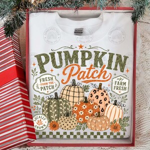 Peut inclure: Un sweat-shirt blanc &agrave; col rond avec le texte PUMPKIN PATCH en vert et orange. Sous le texte se trouvent des illustrations de citrouilles aux motifs vari&eacute;s, dont du tartan, des taches de l&eacute;opard et des fleurs, entour&eacute;es de feuilles vertes.