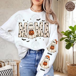 Puede incluir: Una sudadera blanca de manga larga con la palabra MAMA en letras grandes de color beige con lunares negros. Las letras incorporan un fantasma sosteniendo una calabaza. La manga muestra dos ilustraciones de fantasmas con calabazas y la palabra NAME.