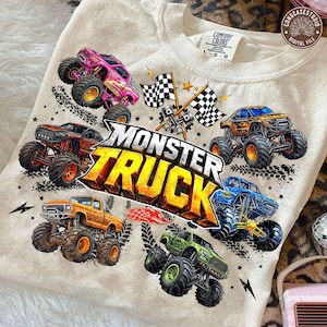 Puede incluir: Camiseta color crema con un gr&aacute;fico vibrante de varios monster trucks en varios colores, incluyendo rosa, naranja, azul y verde. El dise&ntilde;o incluye el texto "MONSTER TRUCK" en letras 3D en negrita, banderas a cuadros y huellas de neum&aacute;ticos.