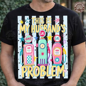 Pode incluir: Uma t-shirt preta com um gráfico de três bombas de gasolina de estilo vintage em rosa, turquesa e rosa. O texto "THIS IS MY HUSBAND'S GAS PROBLEM" está escrito em letras amarelas. O fundo tem riscas verticais brancas, pontos pretos e estrelas.