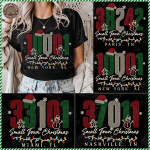 May include: A black t-shirt featuring a graphic design with the text "10001 Small Town Christmas NEW YORK, AL". The design includes large numbers in red, green, and white, a Santa hat, a gingerbread man, a snowman, and colorful string lights.