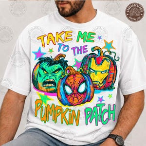 Puede incluir: Una camiseta blanca con un estampado gráfico de tres calabazas estilizadas como superhéroes. El texto "TAKE ME TO THE PUMPKIN PATCH" aparece en letras coloridas. El diseño incluye detalles en verde, rojo y azul con formas de estrellas.