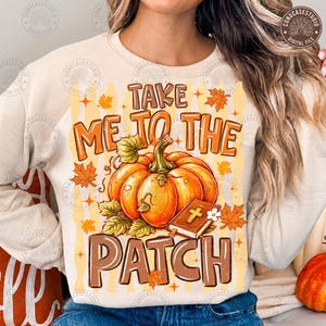 Könnte beinhalten: Ein cremefarbenes Sweatshirt mit Rundhalsausschnitt und einem Grafikdruck, der einen großen orangefarbenen Kürbis und ein kleines braunes Buch mit einem Kreuz zeigt. Der Text "TAKE ME TO THE PATCH" ist in Braun gehalten und von Herbstblättern umgeben.