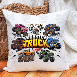 Puede incluir: Coj&iacute;n blanco con un dise&ntilde;o de cami&oacute;n monstruo colorido. El dise&ntilde;o incluye m&uacute;ltiples camiones monstruo en varios colores, las palabras "MONSTER TRUCK", banderas a cuadros y estrellas. El coj&iacute;n est&aacute; sobre una superficie de madera.
