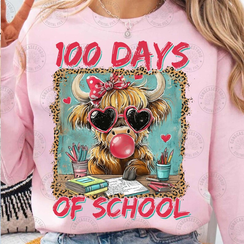 May include: Pink sweatshirt with a colourful graphic. The graphic features a Highland cow wearing heart-shaped sunglasses and blowing a bubble. The text "100 DAYS OF SCHOOL" is above and below the cow.