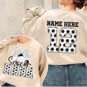 K&ouml;nnte beinhalten: Beigefarbener Sweatshirt mit einem Fu&szlig;ball-Design und dem Text "Soccer Mama" auf der Vorderseite. Die R&uuml;ckseite des Sweatshirts hat ein Fu&szlig;ball-Design mit der Nummer "12" und dem Text "NAME HERE".