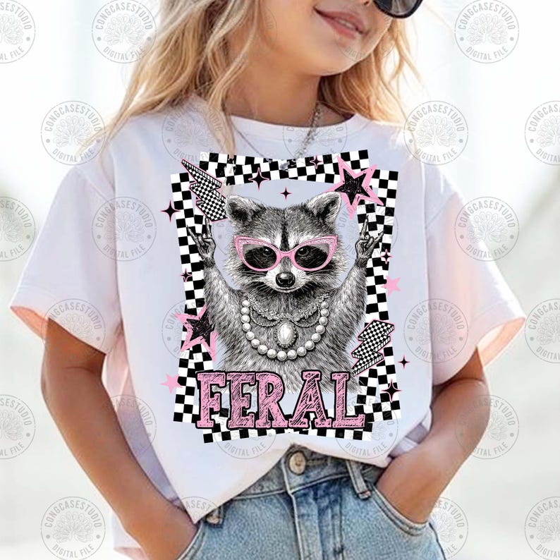 May include: White t-shirt featuring a raccoon wearing pink sunglasses and a pearl necklace. The raccoon is in a checkered frame with pink stars and lightning bolts. The word "FERAL" is printed in pink below the raccoon.