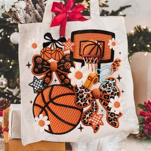 May include: A cream tote bag with a basketball design. The design includes an orange basketball, a hoop, bows, stars, and daisies. A red bow is at the top. The bag has the text "CONGCASES STUDIO DIGITAL FILE".