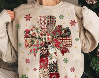 Op de afbeelding: Beige sweatshirt met een patchwork kruisontwerp en een strik. Het kruis is gemaakt van stoffen met rode, groene en witte patronen. Gouden sneeuwvlokken en sterren zijn rond het kruis verspreid. Sweatshirt met lange mouwen.