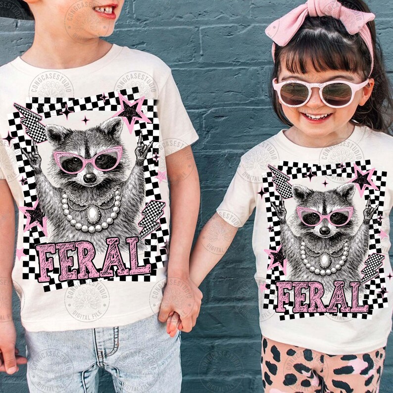 May include: Off-white t-shirts featuring a raccoon wearing pink sunglasses and a pearl necklace. The raccoon graphic is set within a black and white checkered frame with pink stars and lightning bolts. The word "FERAL" is printed in pink.