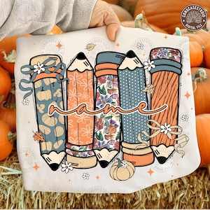 May include: A cream-colored pencil-themed design featuring five pencils with fall-themed patterns and a cursive "name" in the center. The pencils have pumpkin, floral, and dotted patterns, with ribbons and flowers.